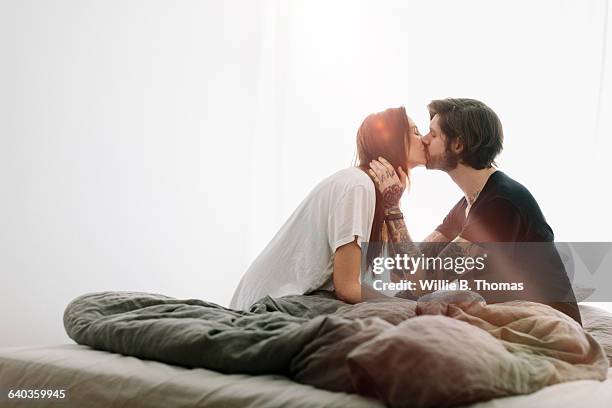 a young couple kissing in bed - good morning kiss images stock-fotos und bilder