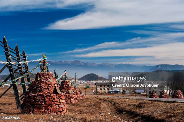 the long road with red stone and prayer flags cross the dried meadow farmland surrounding with high mountains in shangri-la, china. - tibetan culture stock pictures, royalty-free photos & images