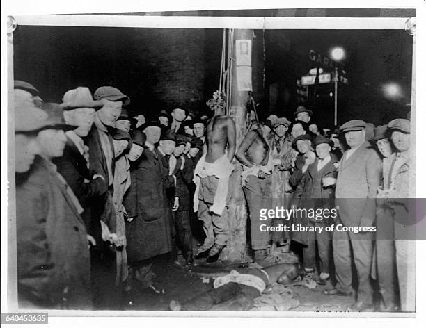 Three lynched African American men surrounded by a crowd of caucasian witnesses.