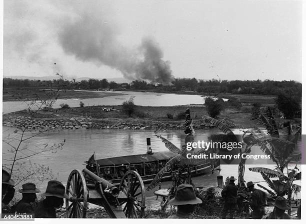 American soldiers watch a boat on a river during the Philippine Insurrection, an uprising in response to America's colonization of the area following...