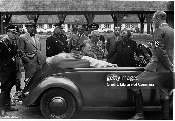 Hermann Goering sits in the backseat of a Volkswagen convertible at Carinhall hunting lodge, surrounded by Nazi officials.