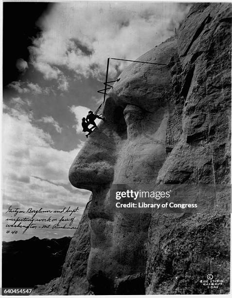 Gutzon Borglum and another man hang from the sculpted forehead of President George Washington on Borglum's famous monumental sculpture at Mount...