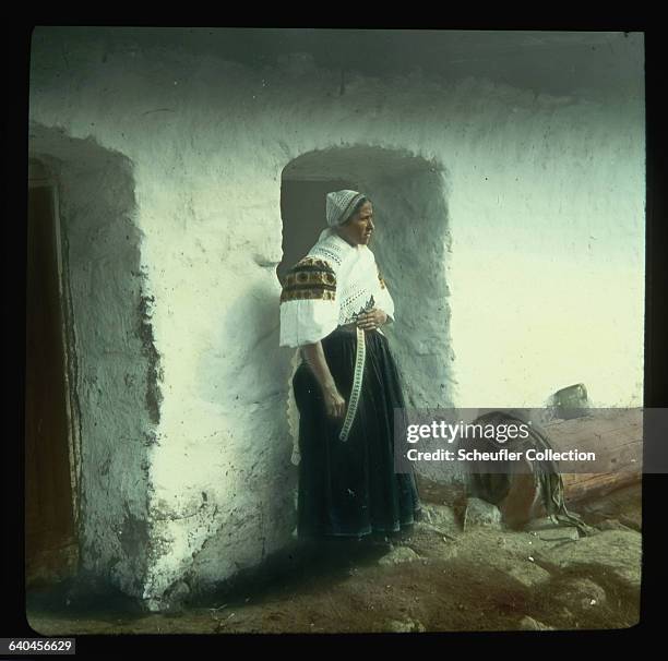 Slovakian peasant farmer, wearing traditional dress, stands outside her home in Detva.