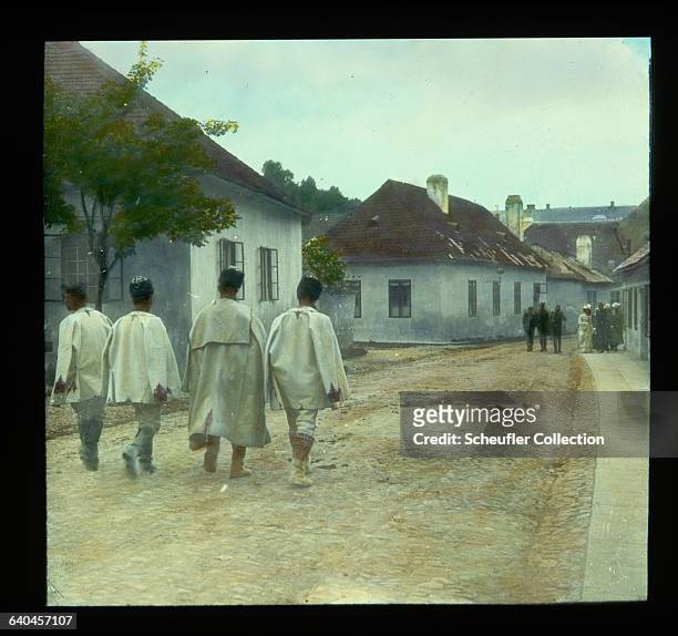 Men wearing traditional dress walk along a village street in Detva, Slovakia.