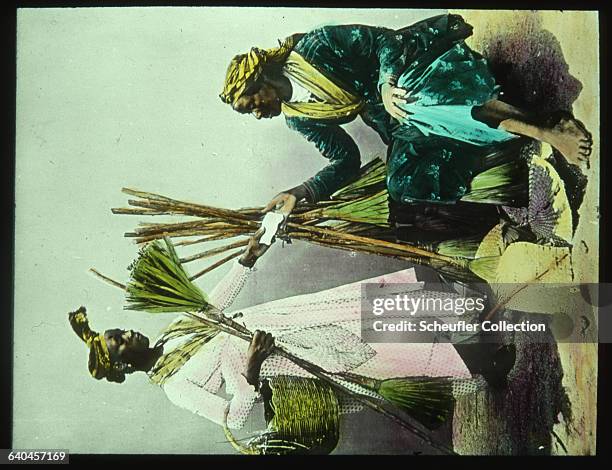 Two women trade brooms in Guadeloupe.