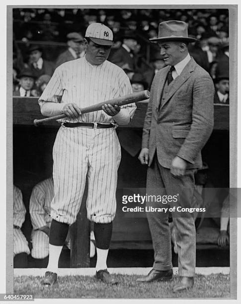 Babe Ruth holds up his bat in front of a man in a suit, before the start of a Yankees-Athletics game at the Polo Grounds in New York.