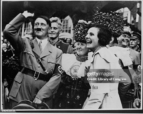 Adolph Hitler gives a Nazi salute, as German men and women look on and laugh.