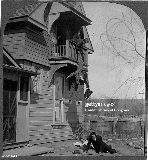 Humorous photo of a mother holding her daughter from a balcony, preventing her elopement with a man sprawled on the ground below.
