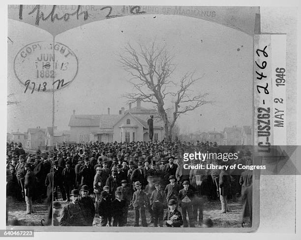 The body of an African American man named MacMannus hangs from a tall tree above a huge crowd of caucasian men. Minneapolis, Minnesota.