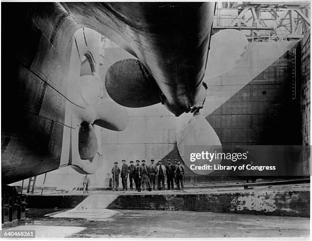 Workers pose near the port and centre propellers of the ocean liner, RMS Olympic, in the Thompson Graving Dock during fitting out at the Harland and...