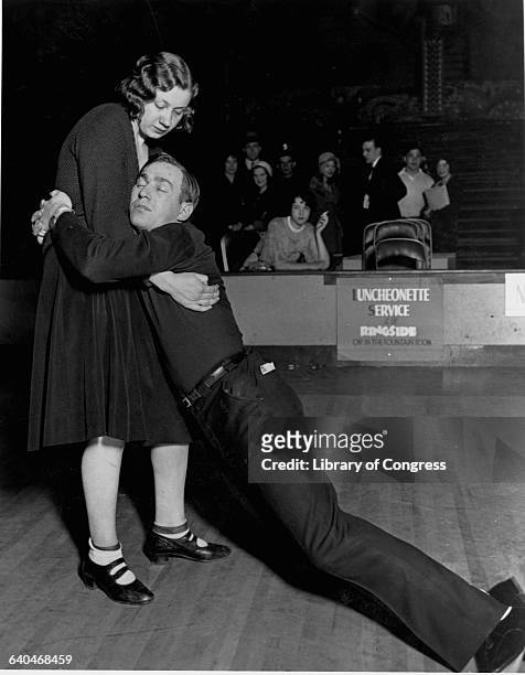 Woman struggles to hold up her sleeping dancing partner during a competition at the Merry Garden Ballroom. Members of the audience watch in the...