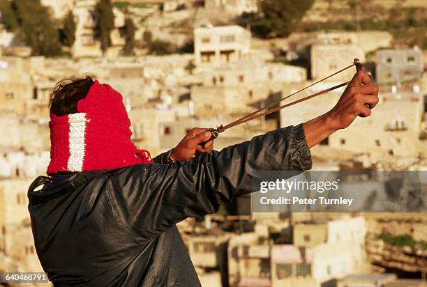 Masked Palestinian man shoots rocks with a slingshot in the battle between Palestinians and Israeli soldiers in the West Bank.