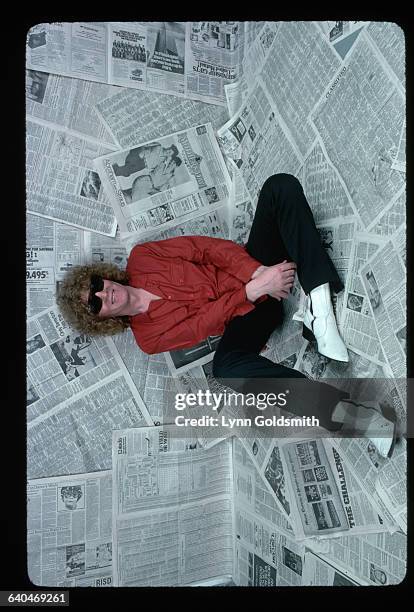 Rock and roll singer/songwriter Ian Hunter is shown seated on newspapers that cover the floor and the wall behind him.