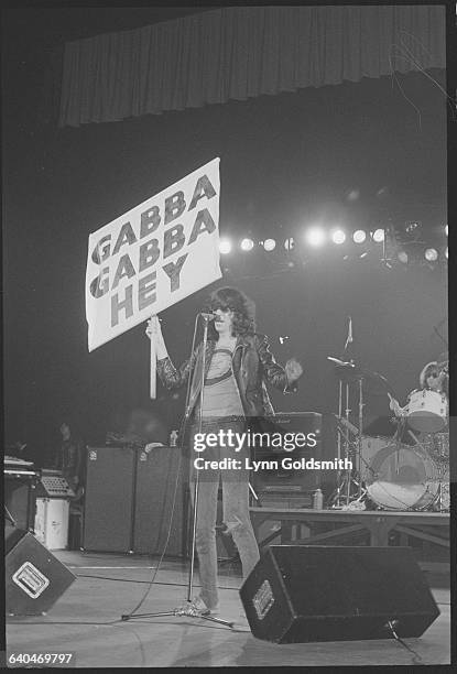 The Romone's lead singer Joey Ramone holds up a sign displaying one of the bands famous chants "Gabba Gabba Hey" while performing on stage.