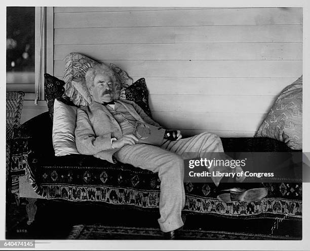 Mark Twain reclines on a sofa with a book.