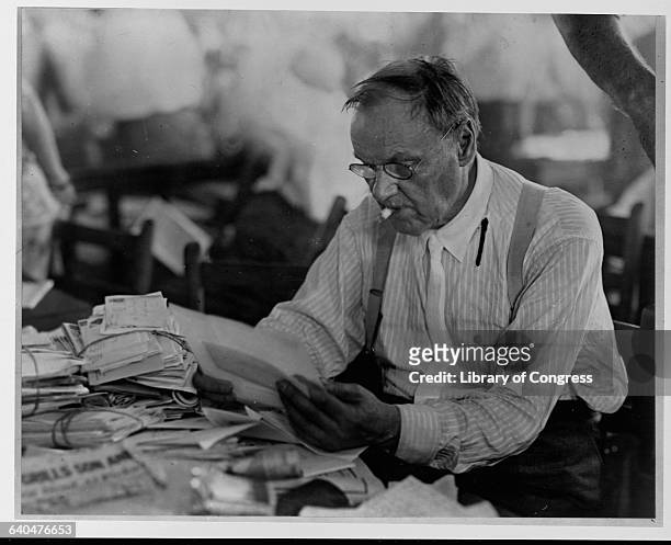 Prominent attorney Clarence Darrow reads a stack of letters in an office.