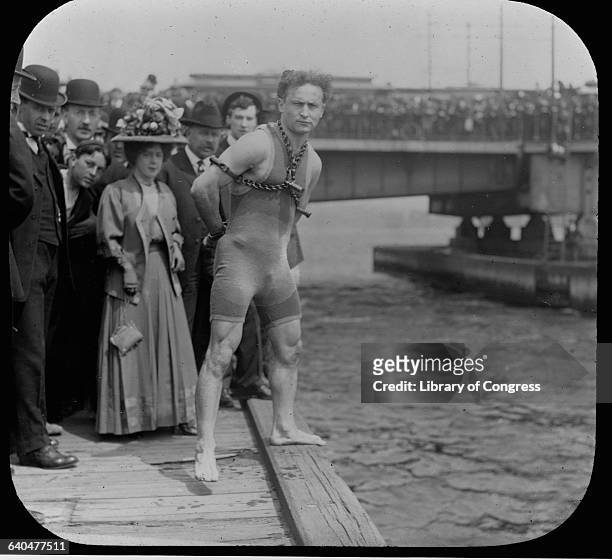 Harry Houdini stands in chains at the edge of a pier ready to dive into the water.