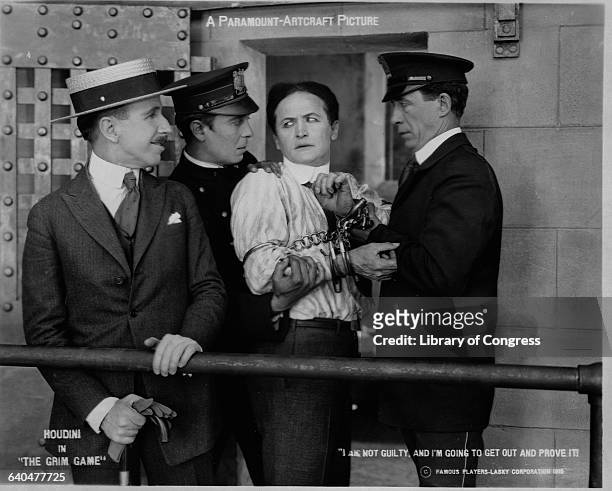 In this photo still from the movie,The Grim Game Houdini with hands shackled and held firmly by two guards looks back at the warden and Vows, "I am...