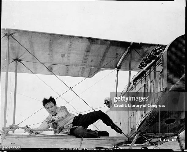 Escapologist Harry Houdini lies on the wing of a Curtis biplane holding on to the wires and a rope in a scene from the film 'The Grim Game', 1919.