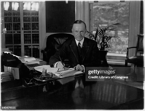 Portrait of President Calvin Coolidge sitting at his desk in the Oval office as he signs a tax bill. Washington DC, August 15, 1923.