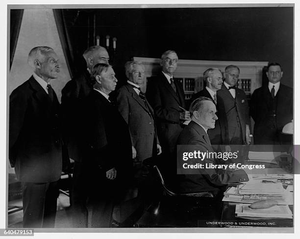 President Calvin Coolidge signs a tax bill in the Oval Office as several congressmen and cabinet members look on. Washington D.C., August 15, 1923.