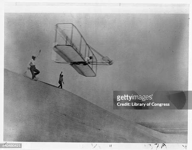 Orville Wright and Dan Tate launch the third Wright Glider into the air, with Wilbur Wright aboard as pilot, at Kill Devil Hill on October 18, 1902....