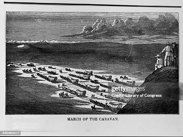 Four men look down from a hill top as several people in covered wagon begin their journey along the Santa Fe Trail.