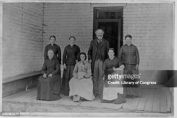 Latter Day Saint poses on a porch with his mother and five wives, 1885.