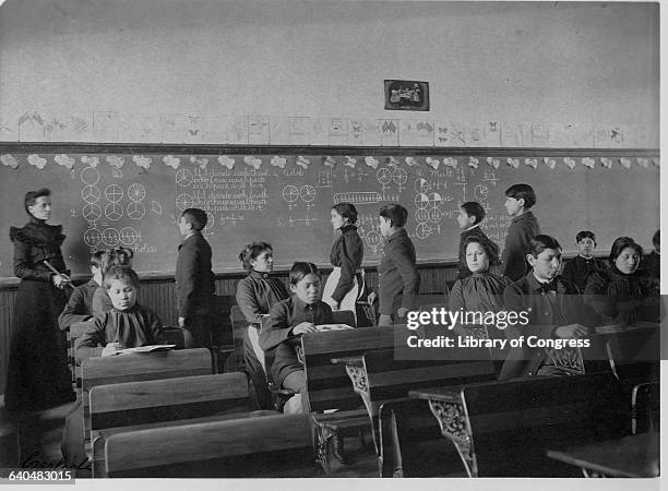 Native Amercian students study at their desks and line up at the chalkboard during class at the Carlisle Indian School, Carlisle, Pennyslvania. |...