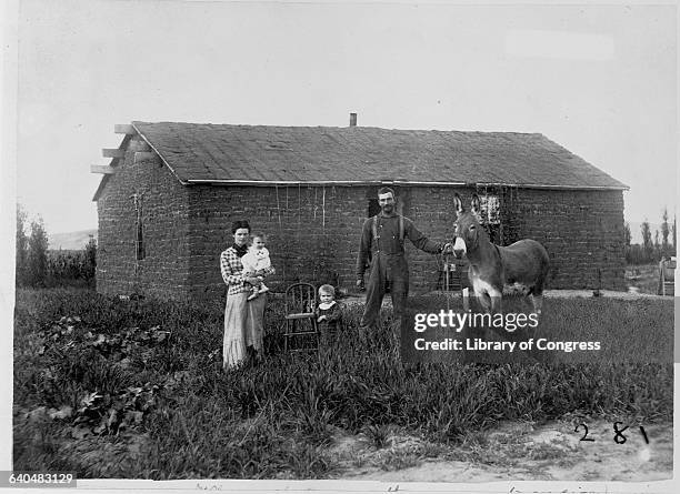 Family stands with a donkey in front of a sod house.