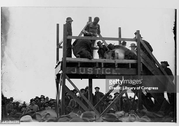 Crowd watches as Caucasian men prepare a platform for the hanging of an African American man named Henry Smith accused of killing a Caucasian girl...