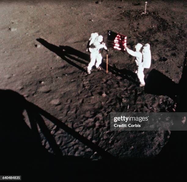 Astronauts Neil Armstrong and Buzz Aldrin place an American flag on the lunar surface. | View from: 'Eagle' Lunar Module.