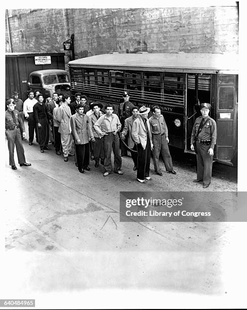 Group of hispanic men dressed in Zoot suits stand chained together as they wait to board a Los Angeles County Sheriffs' bus for a court appearance....