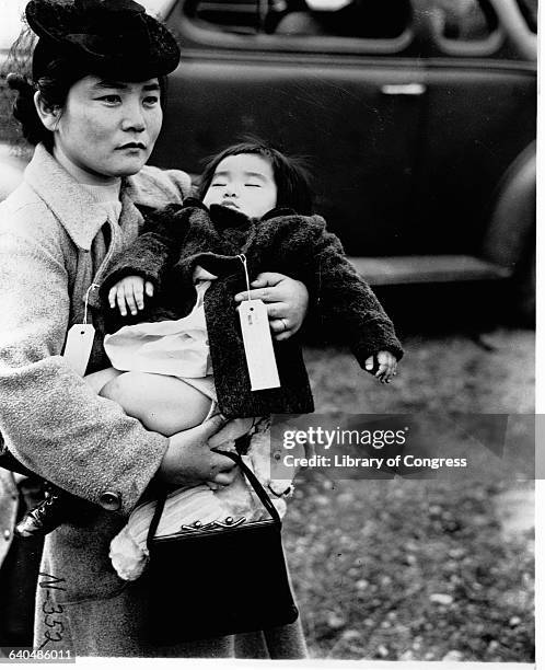 Japanese American woman holds her sleeping daughter as they prepare to leave their home for an internment camp, Bainbridge Island, Seattle 1942....