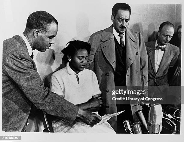 Roy Wilkins, Director of the National Association for the Advancement of Colored People, holds a piece of paper for Autherine Lucy as she speaks at a...