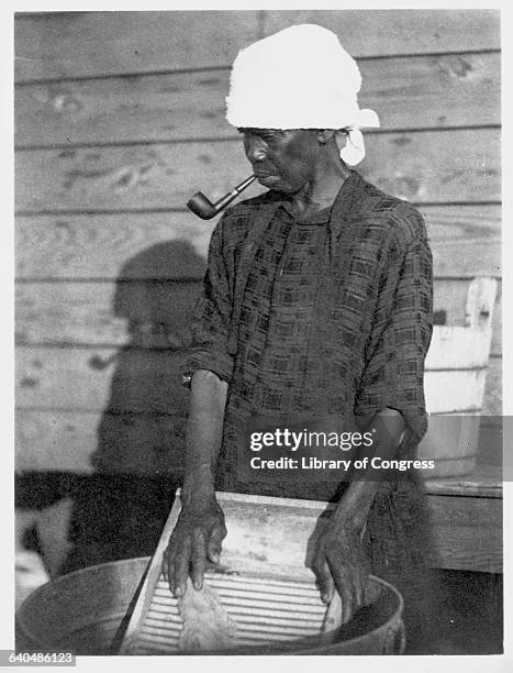 An African American women smokes a pipe while washing clothes on a washboard, 1930.