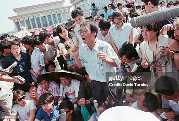 Chinese protester uses a microphone to address the crowd at Tiananmen Square. Several journalists are in the crowd with tape recorders.