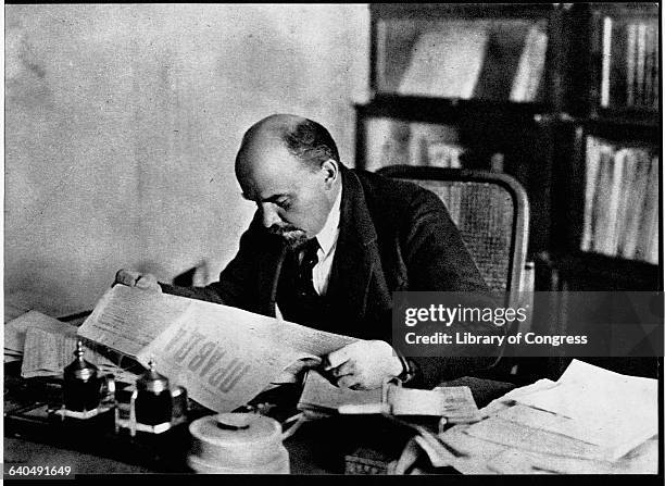 Lenin sits at his desk and reads the newspaper.