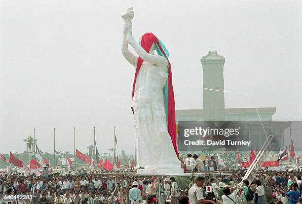 Crowds of people watch the unveiling of the Goddess of Democracy in Tiananmen Square. The Monument to the People's Heroes and Mao Zedong Mausoleum...