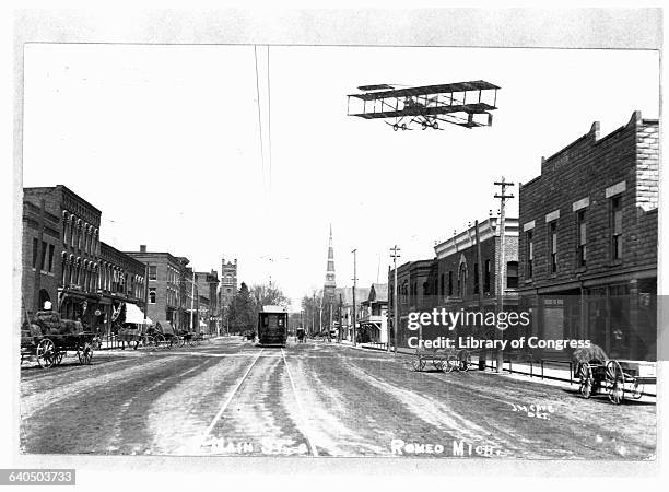 An airplane flies over Romeo, Michigan, as a streetcar runs down Main Street. Ca. 1905. | Location: Romeo, Michigan, USA.