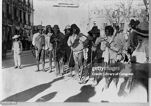 Tarahumara holding switches pose on the side of the street during the Mexican Revolution, 1911-1917.