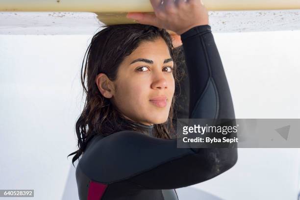 Surfer Girl in Wetsuit Holding Surfboard on her Head