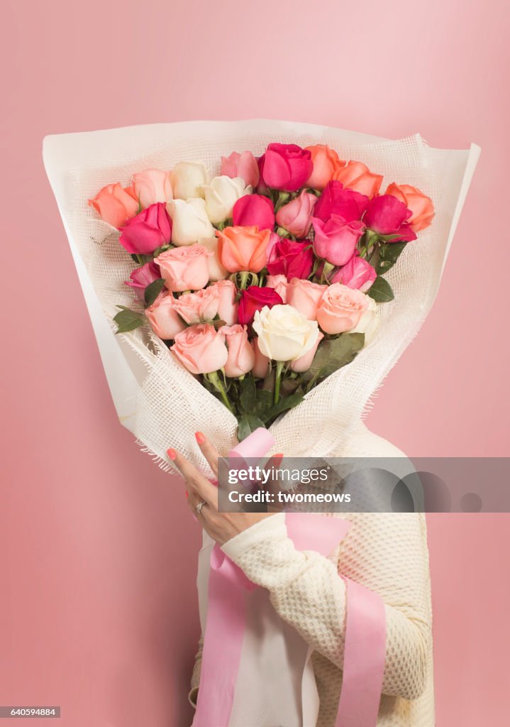Women's holding a big bouquet of roses on pink background.