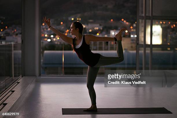 woman stretching onone leg on yoga mat, at sunset - yoga studio stock pictures, royalty-free photos & images