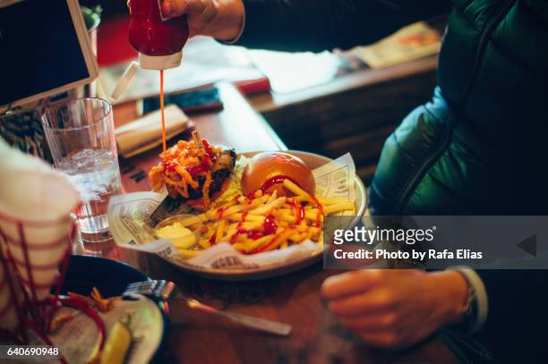 man adding ketchup on burger. - plate eating table imagens e fotografias de stock