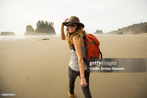 a woman hiking along a remote beach. - mirar por encima del hombro mujer fotografías e imágenes de stock