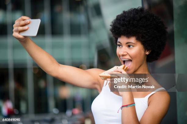 excited teenage girl clicking her picture while biting sandwich. - girls laughing eating sandwich foto e immagini stock