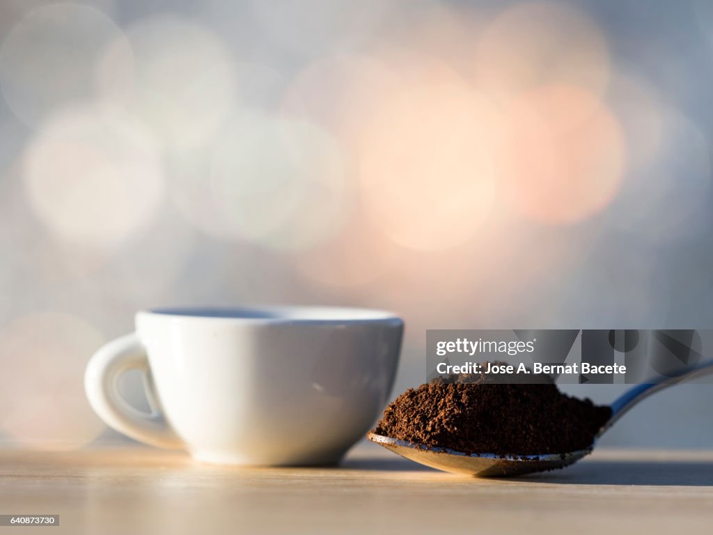 Cup of coffee espresso and teaspoon with a dosis of ground coffeeon a table of wood