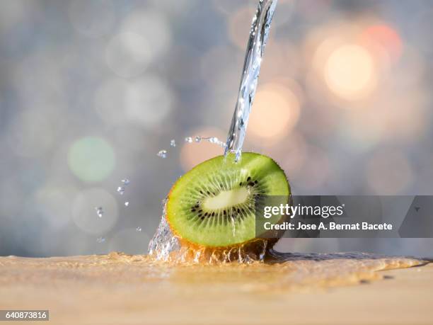 kiwi fruit, under a jet of clean and fresh water, illuminated by the light of the sun - squirting stock pictures, royalty-free photos & images