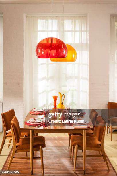 a women setting a colorful table in a  bright midcentury modern dining room - eetkamer stockfoto's en -beelden
